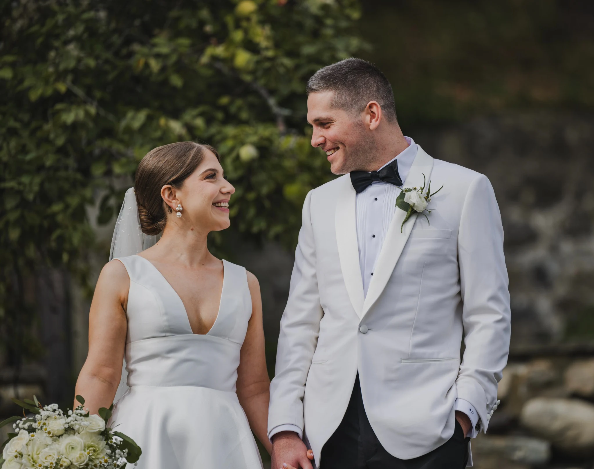 Bride and groom smiling at each other, with the groom wearing an ivory dinner jacket